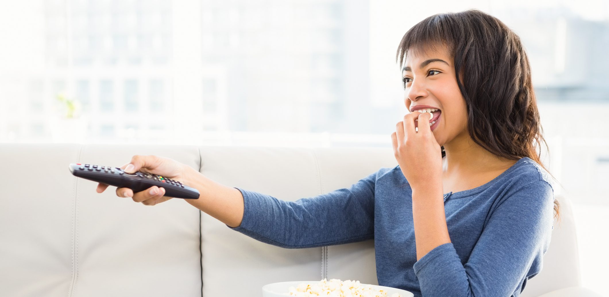 Smiling casual woman watching tv with popcorn at home
